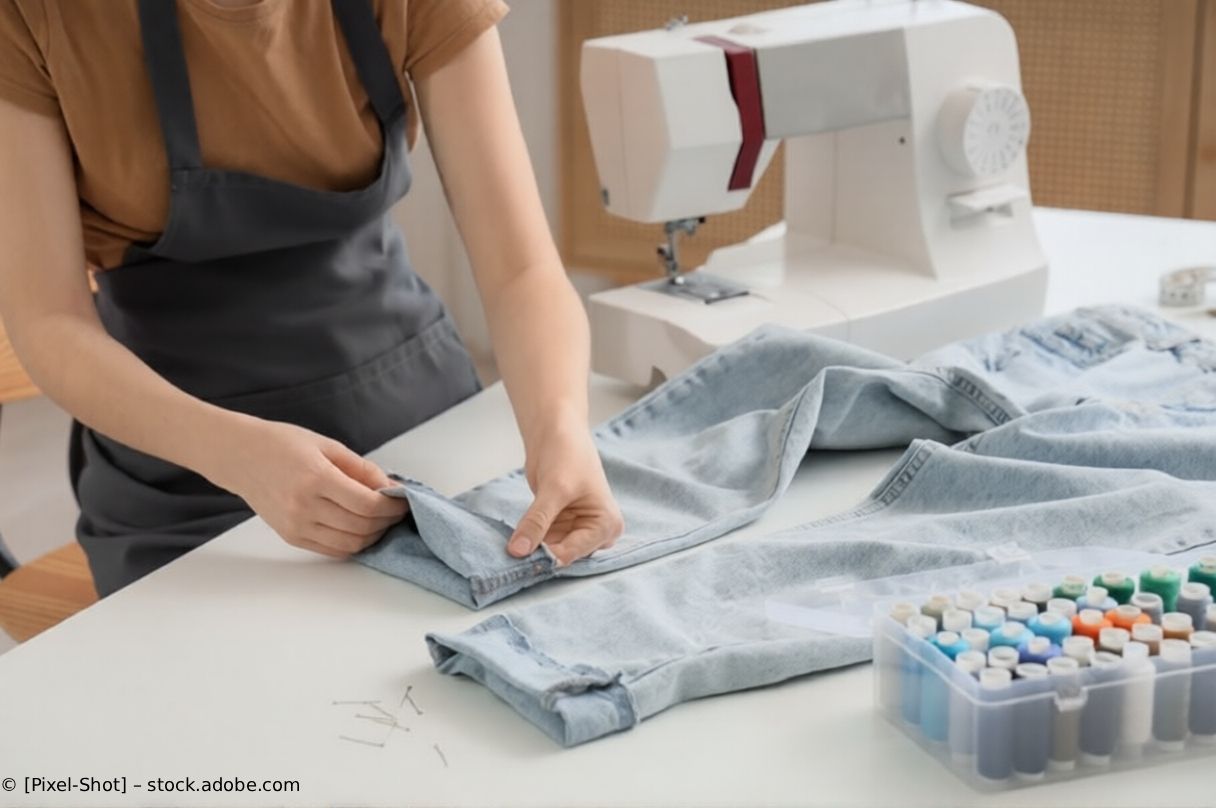 Eine Person näht hellblaue Jeans neben einer weißen Nähmaschine auf einem Tisch.