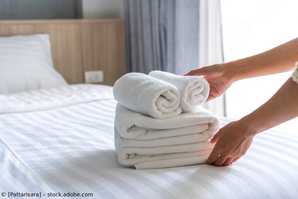 Hände stapeln gefaltete weiße Handtücher auf einem Bett in einem hellen Schlafzimmer