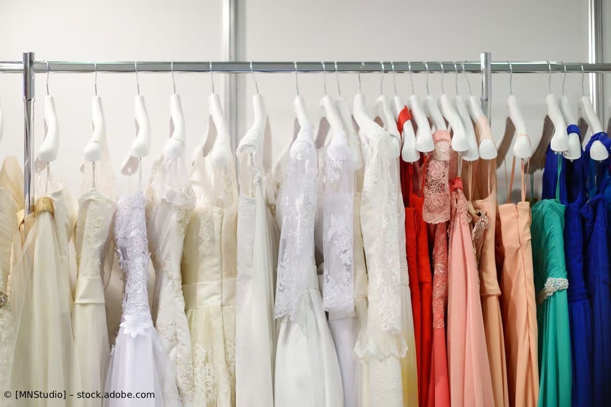 Eine Reihe hängender Abendkleider in Weiß, Rot, Rosa, Türkis und Blau an einer Kleiderstange