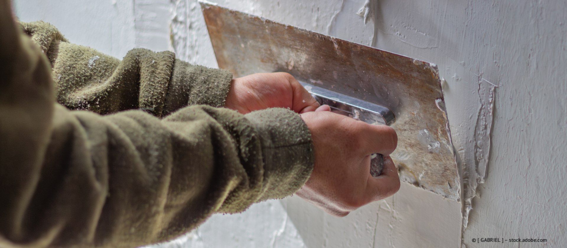 Person using a trowel to apply plaster to a wall.