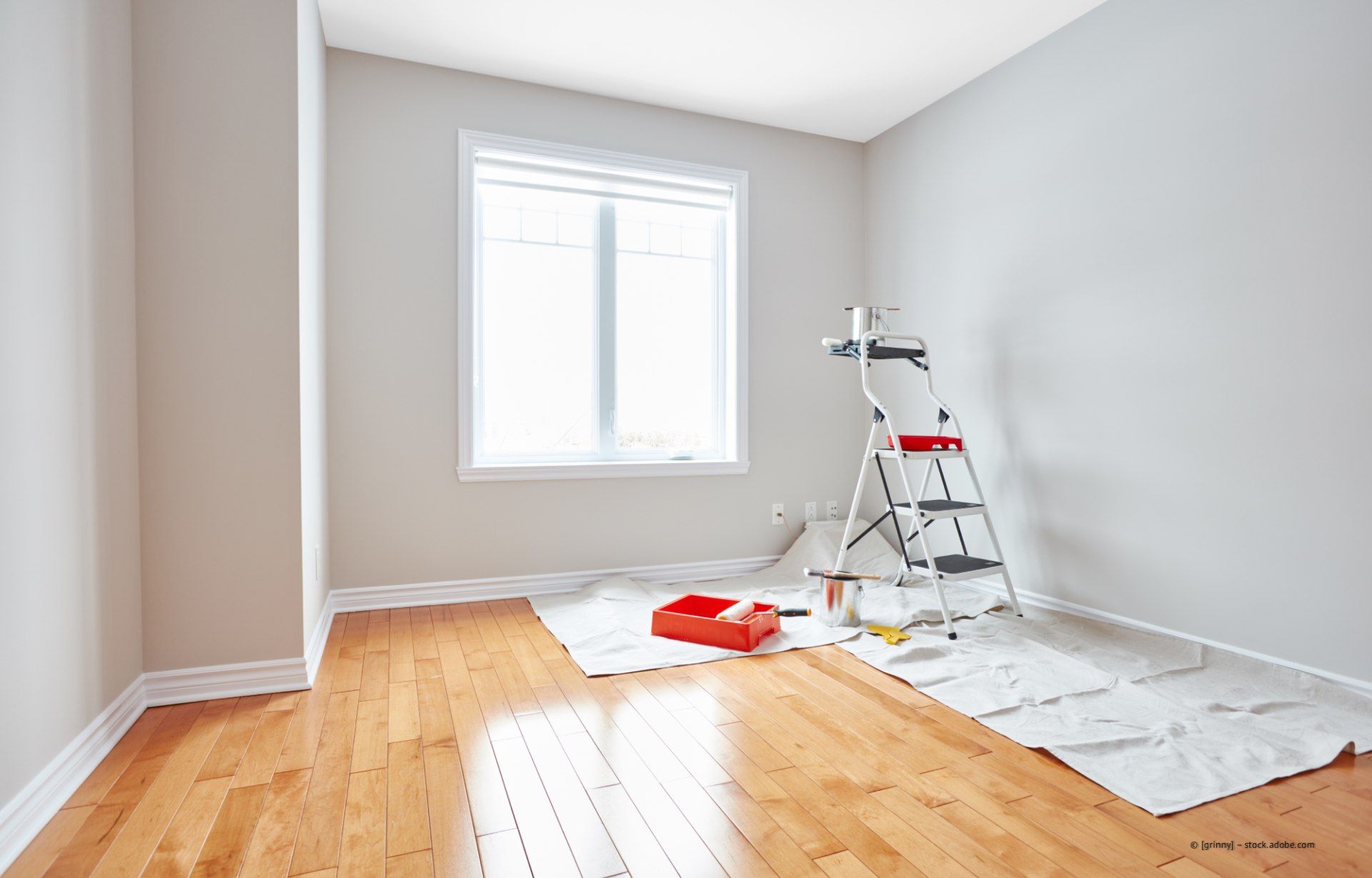Empty room with hardwood floors and freshly painted walls; a ladder and painting supplies are present near a window.