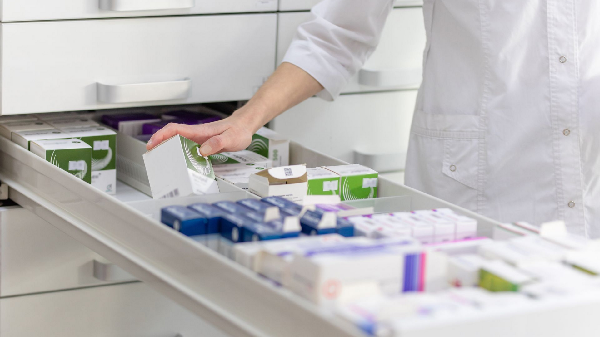 La main d'un pharmacien plongeant dans un tiroir rempli de boîtes de médicaments dans une pharmacie.