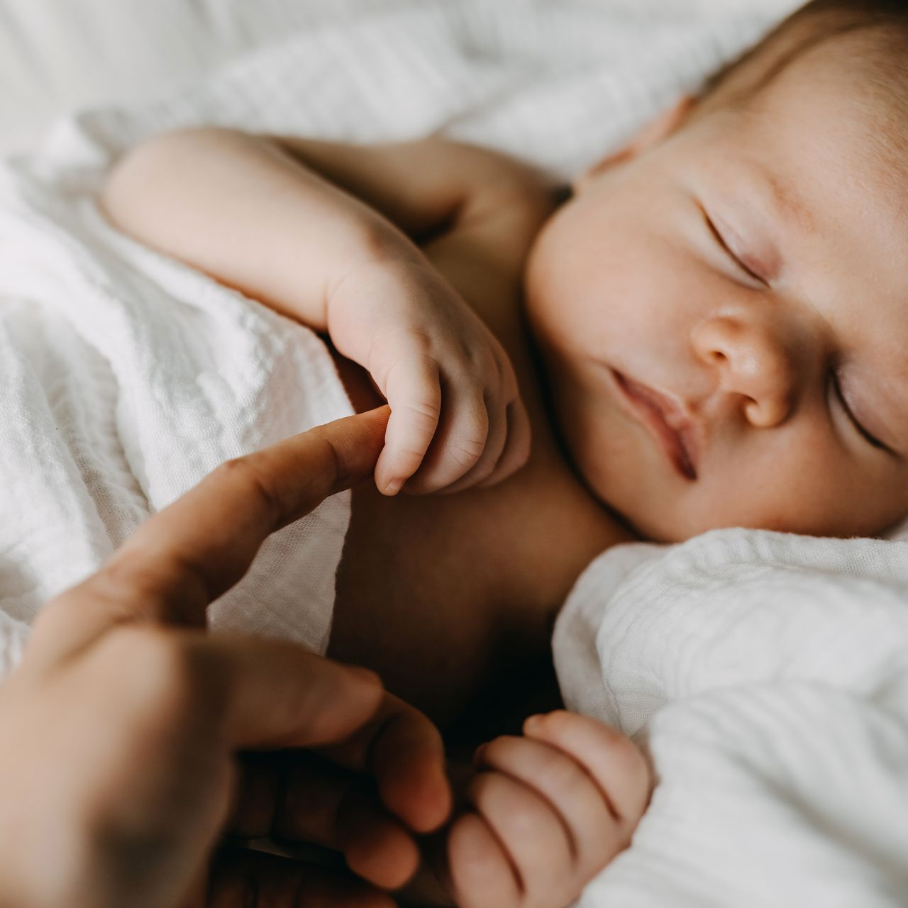 Un nouveau-né dort, une main touchant doucement sa petite main sur la literie blanche.