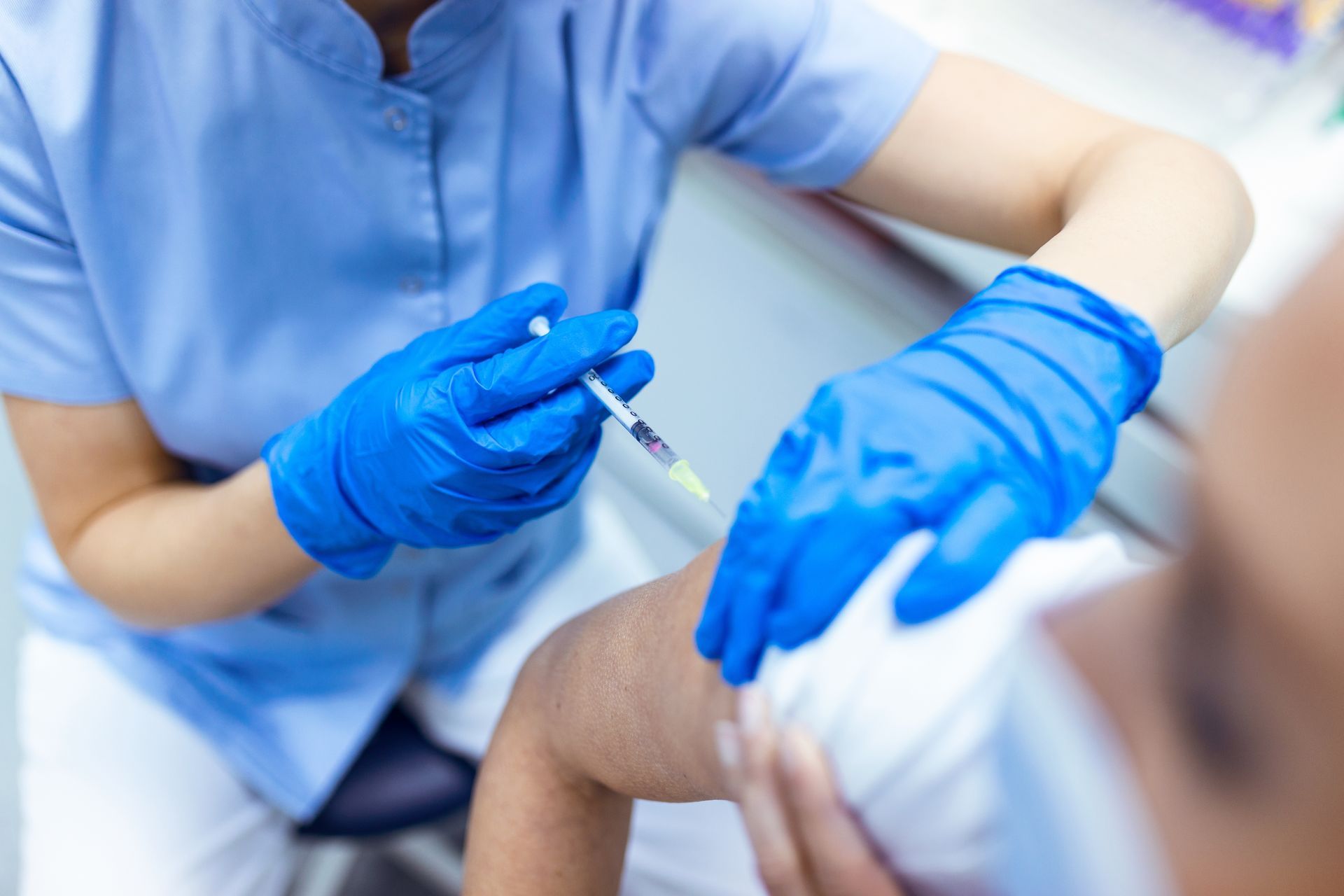 Une infirmière portant des gants bleus administre une piqûre au bras d'un patient.