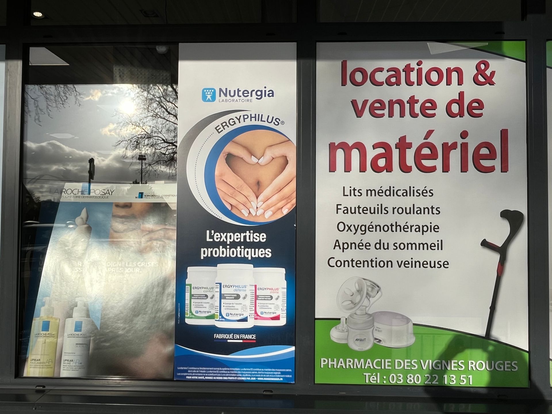 Vitrine de pharmacie avec publicités pour la location de probiotiques et de matériel médical.