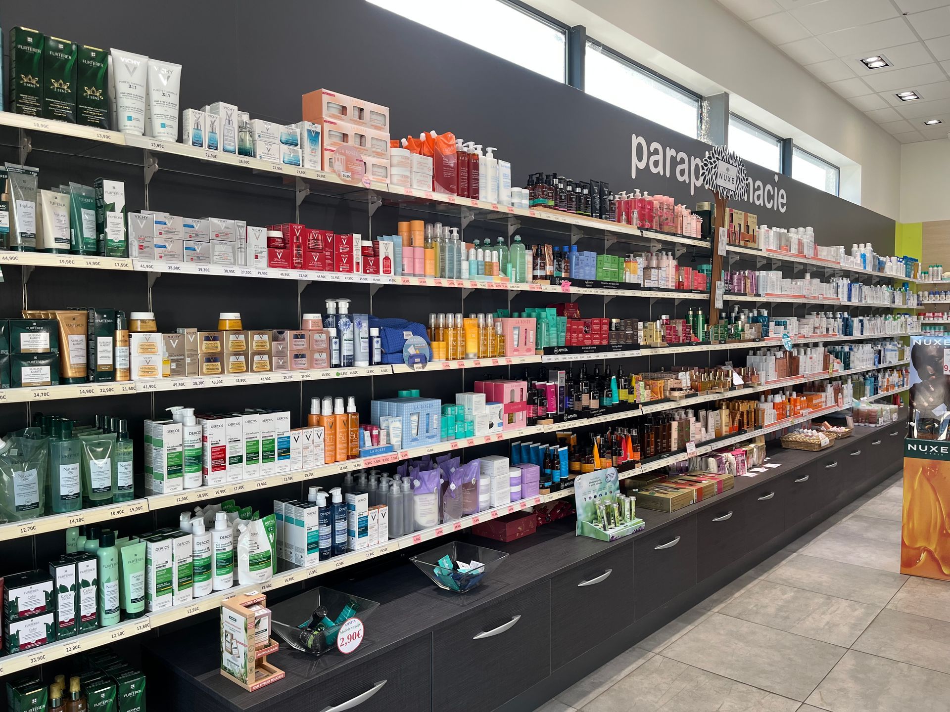 Des étagères remplies de produits de soins de la peau et de beauté dans une pharmacie, étiquetées « parafarmacia ».