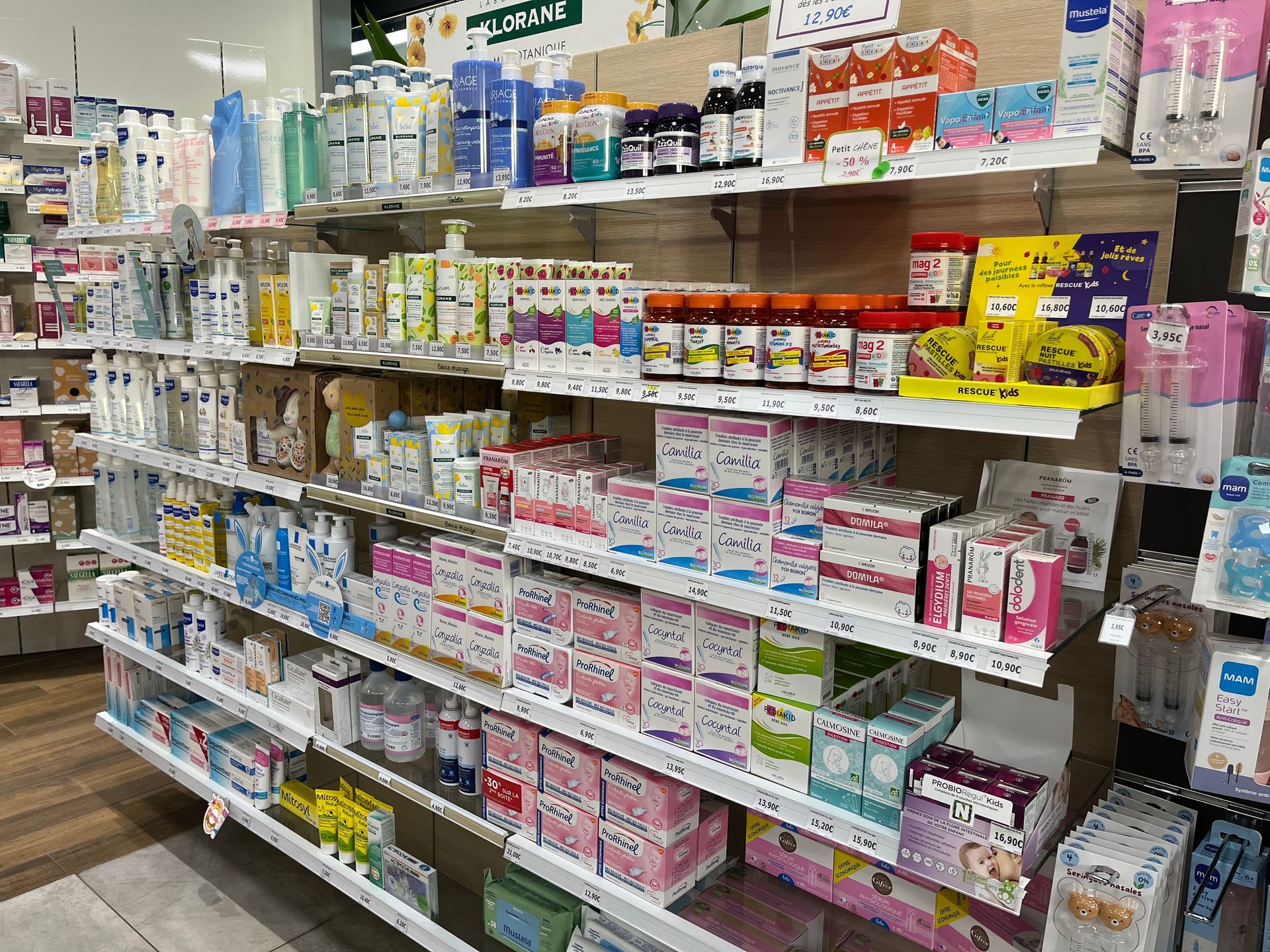 Étagères dans une pharmacie, remplies de divers produits de santé et pour bébés dans des emballages colorés.