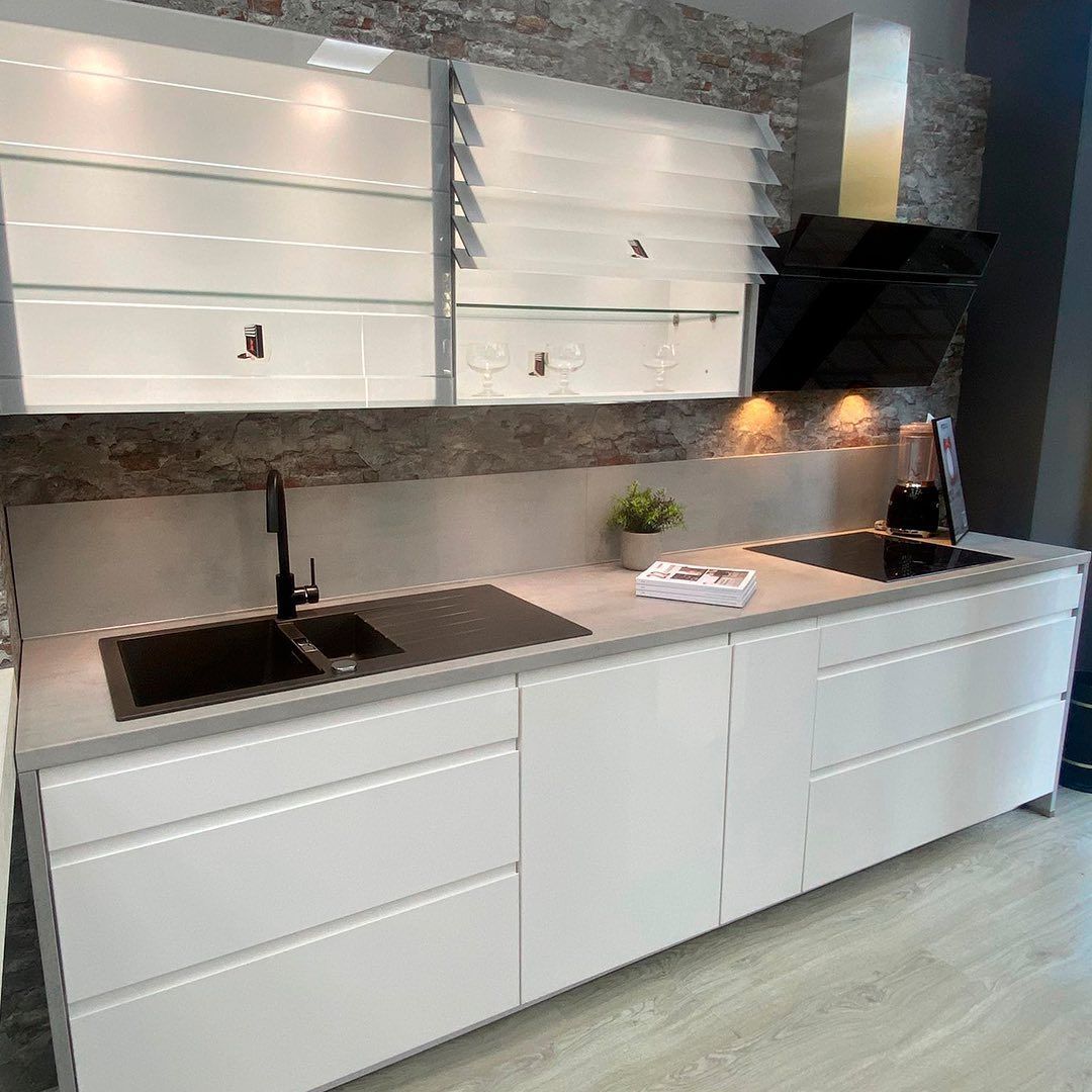 Una cocina con gabinetes blancos, un fregadero, una estufa y una campana extractora.