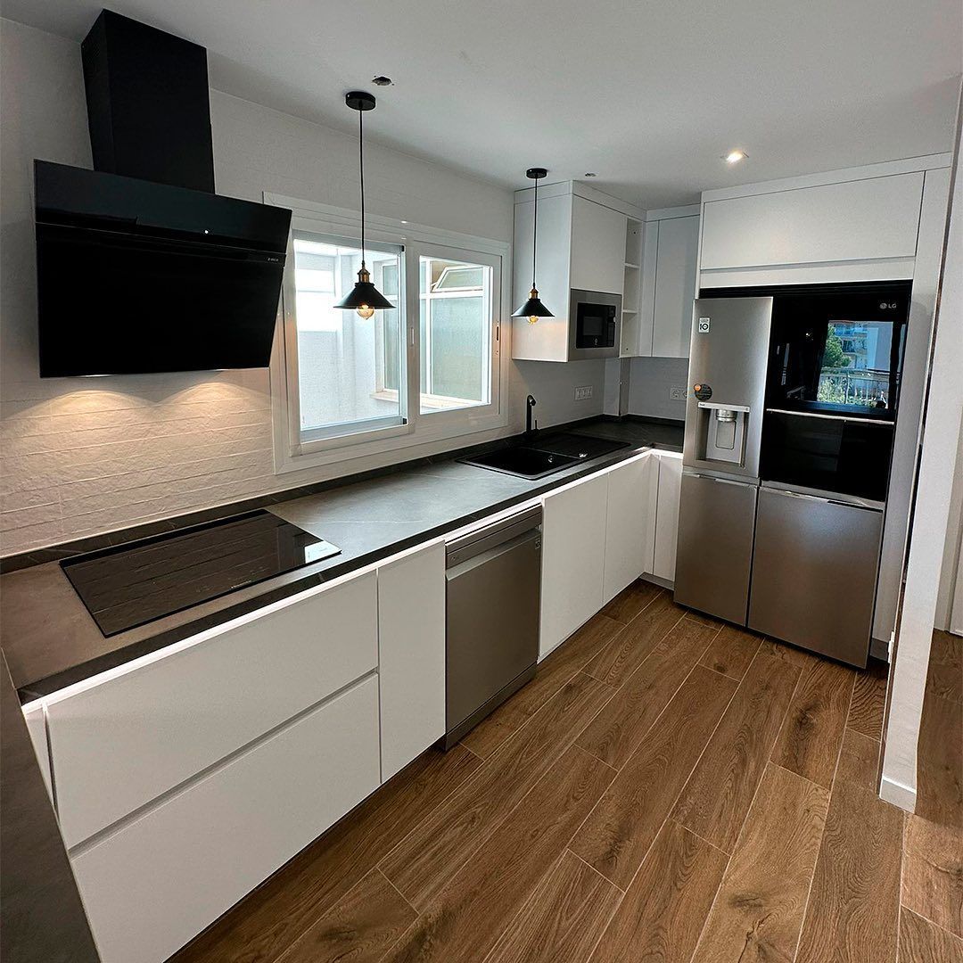 Una cocina con gabinetes blancos y electrodomésticos de acero inoxidable y piso de madera.