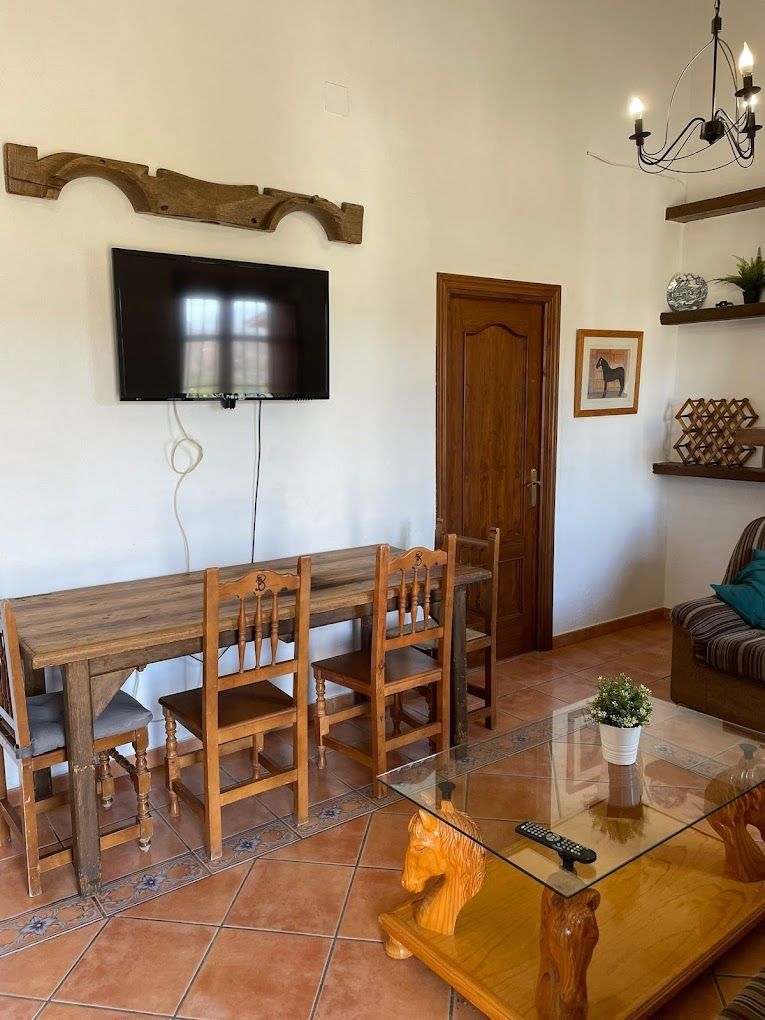 Una sala de estar con una mesa, sillas, una mesa de café y un televisor de pantalla plana.