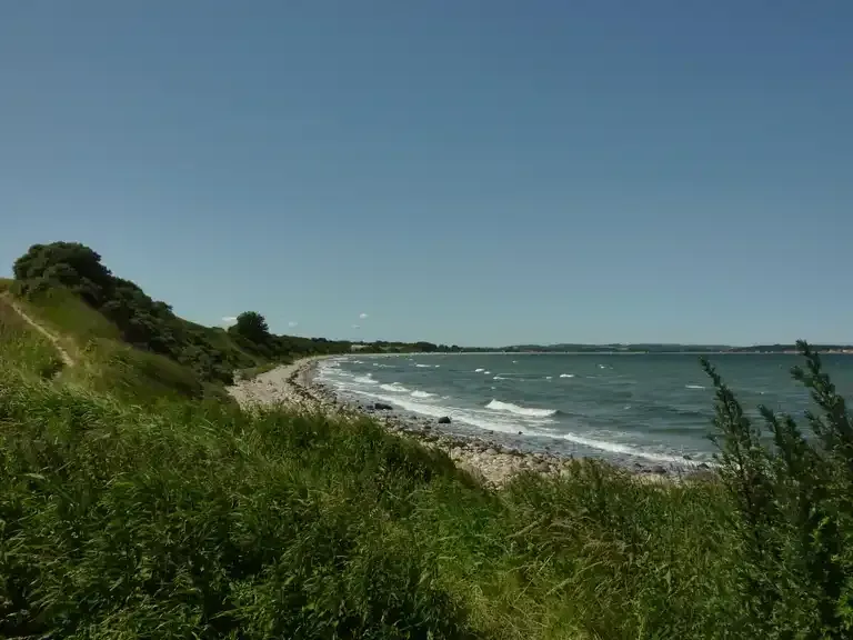 Ein Blick auf einen Strand von einem grasbewachsenen Hügel an einem sonnigen Tag.