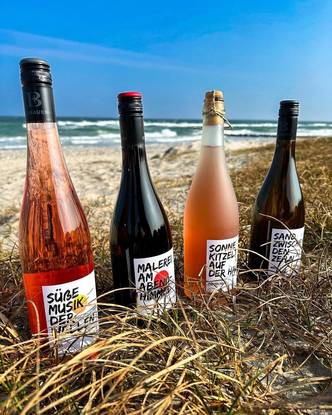 Vier Flaschen Wein stehen auf einem Heuhaufen an einem Strand.
