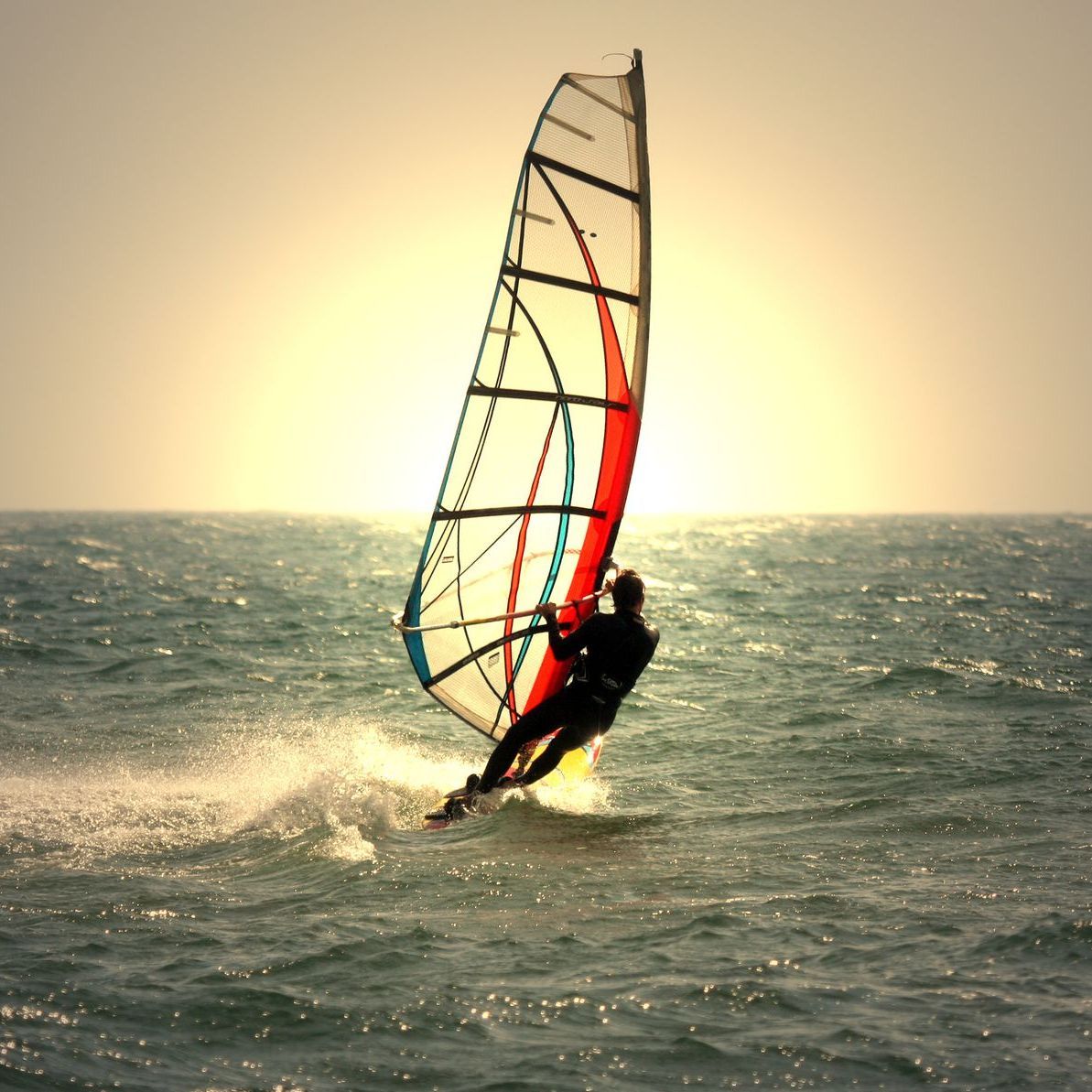 A man is windsurfing in the ocean at sunset