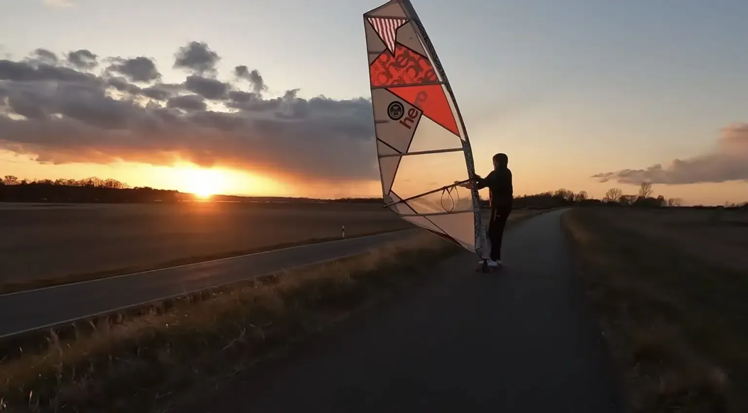 Eine Person hält bei Sonnenuntergang am Straßenrand ein Segel.