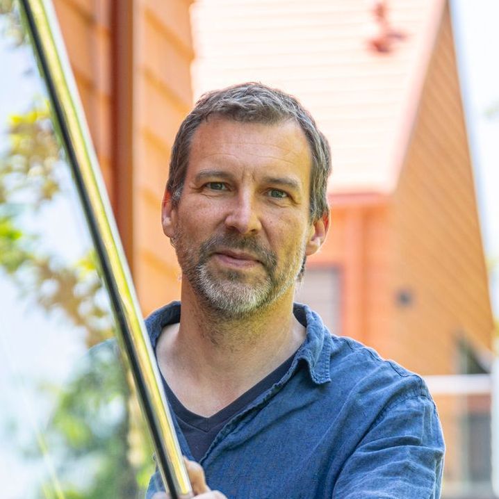 A man with a beard is holding a pole in front of a building.