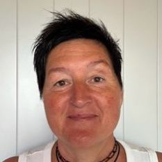 A woman wearing a white tank top and a necklace is smiling for the camera.