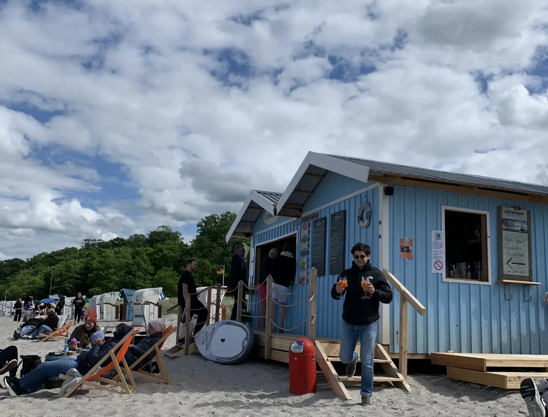 Ein Mann steht vor einem blauen Strandhaus an einem Strand.
