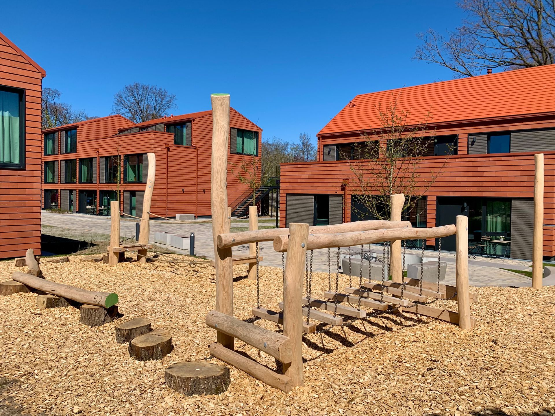 Ein Holzspielplatz vor einem Gebäude mit rotem Dach.