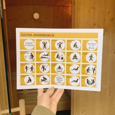 Eine Person hält ein Schild mit der Aufschrift „Sauna-Baderegeln“