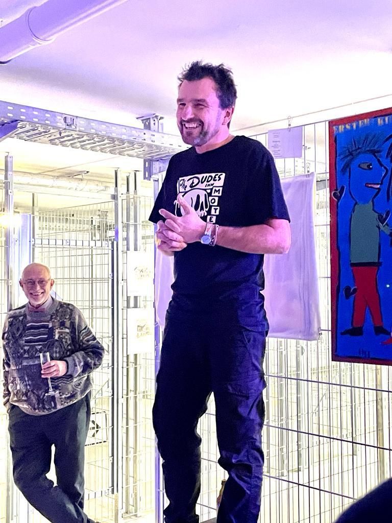 Ein Mann in einem schwarzen Shirt steht vor einem Gemälde.