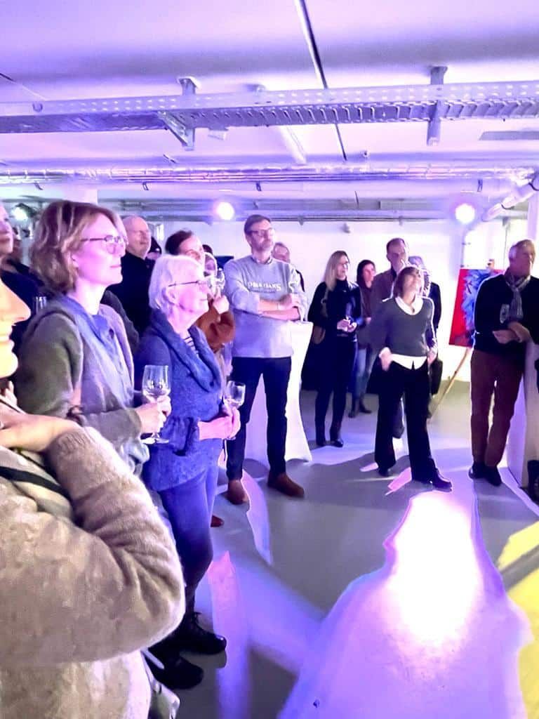 Eine Gruppe von Menschen steht mit Weingläsern in den Händen in einem Raum.