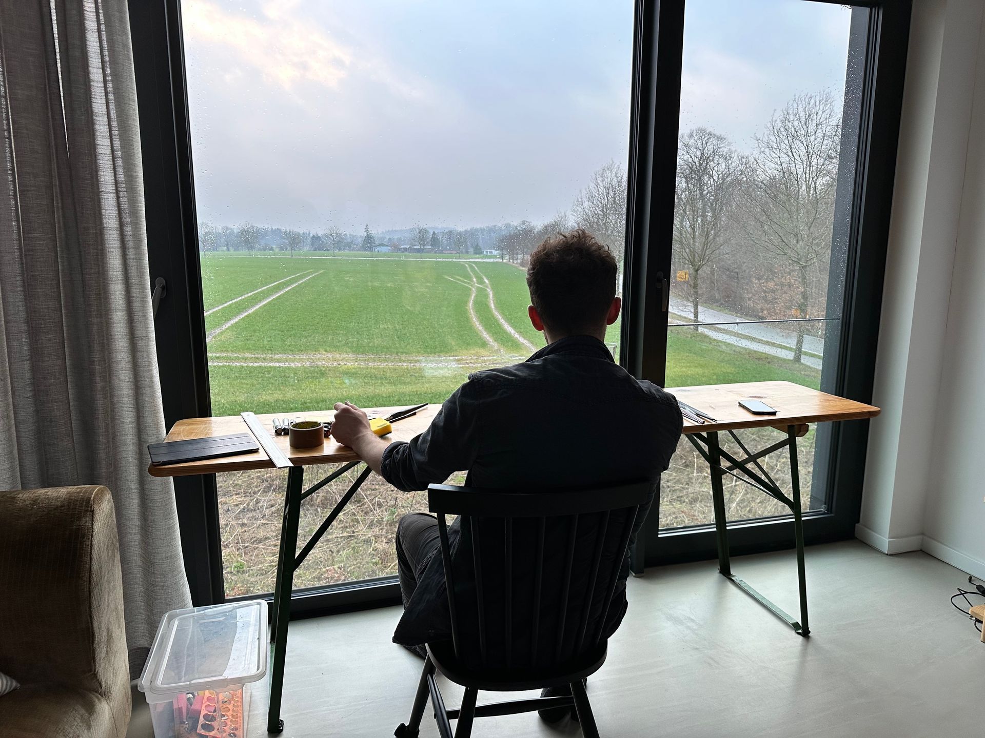 Ein Mann sitzt an einem Schreibtisch vor einem großen Fenster und blickt hinaus.