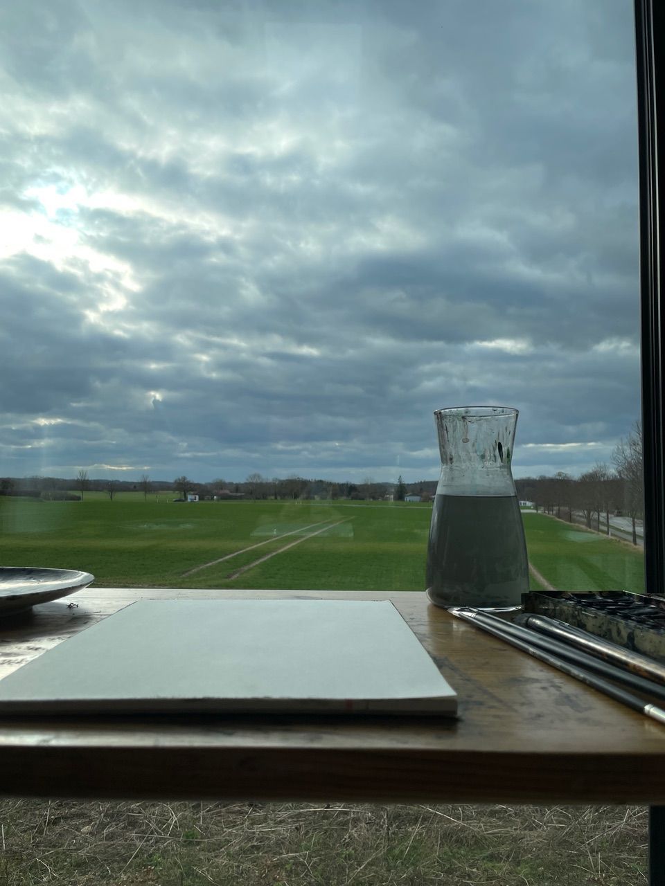 Ein Laptop steht auf einem Holztisch vor einem Fenster mit Blick auf ein Feld.