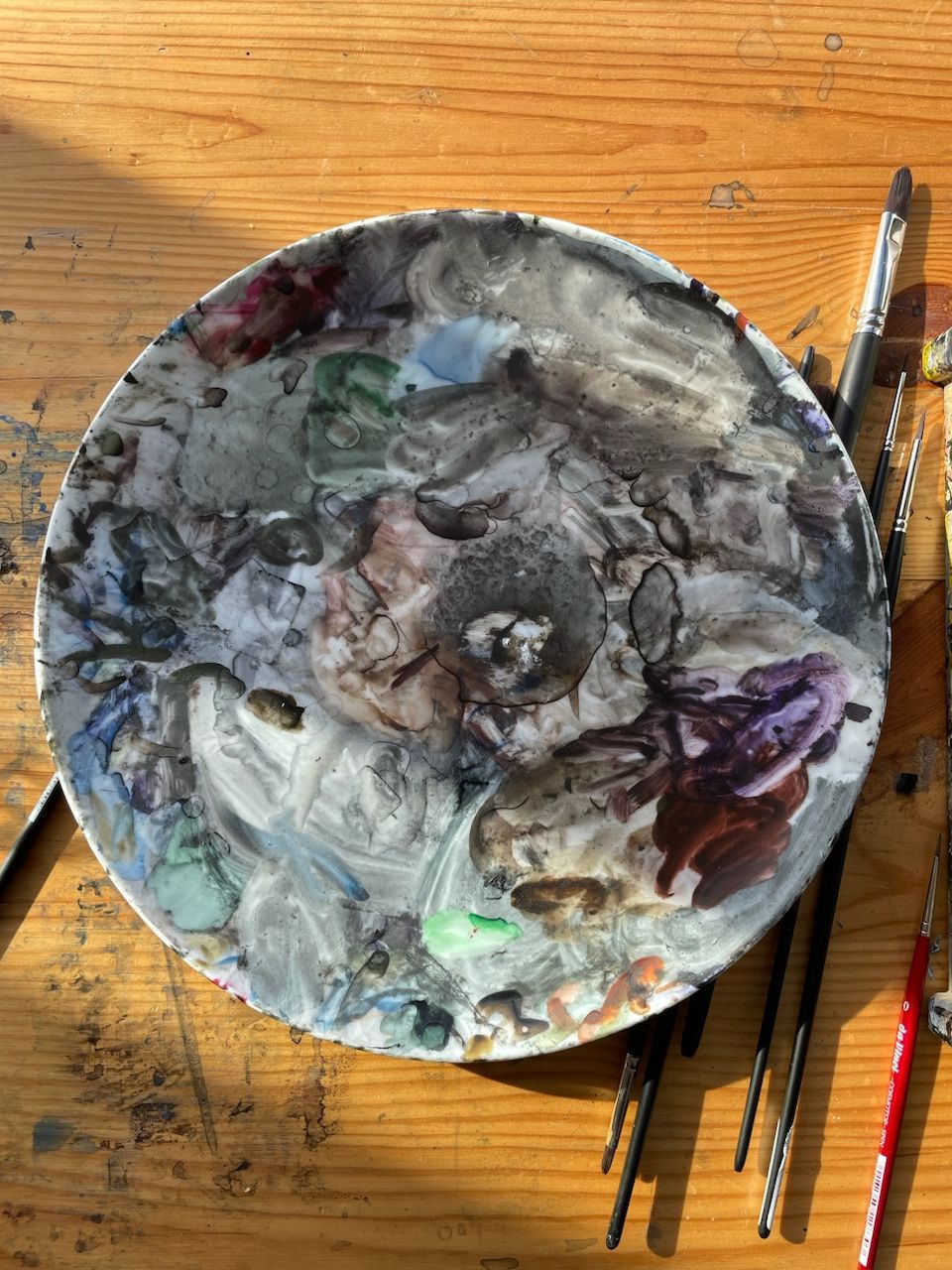 Eine Malpalette steht neben Pinseln auf einem Holztisch.