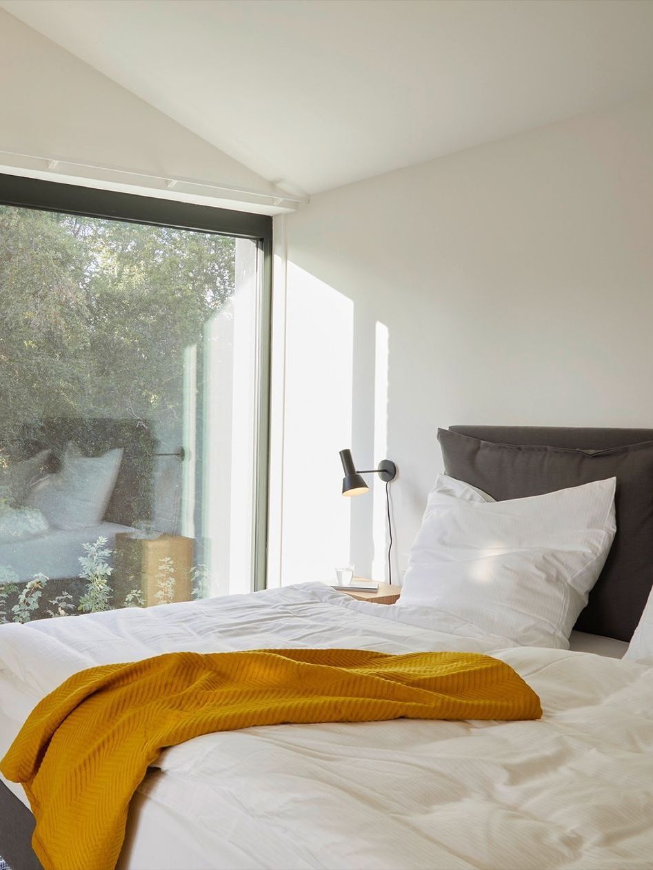 A bedroom with a large window and a bed with a yellow blanket on it.