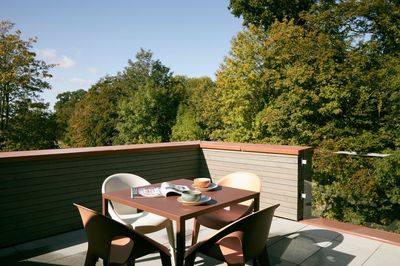 Ein Tisch und Stühle auf einem Balkon einer Ferienwohnung in Hohwacht mit Bäumen im Hintergrund.