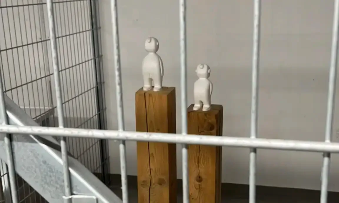 Zwei Statuen sitzen auf Holzsäulen hinter einem Metallzaun.