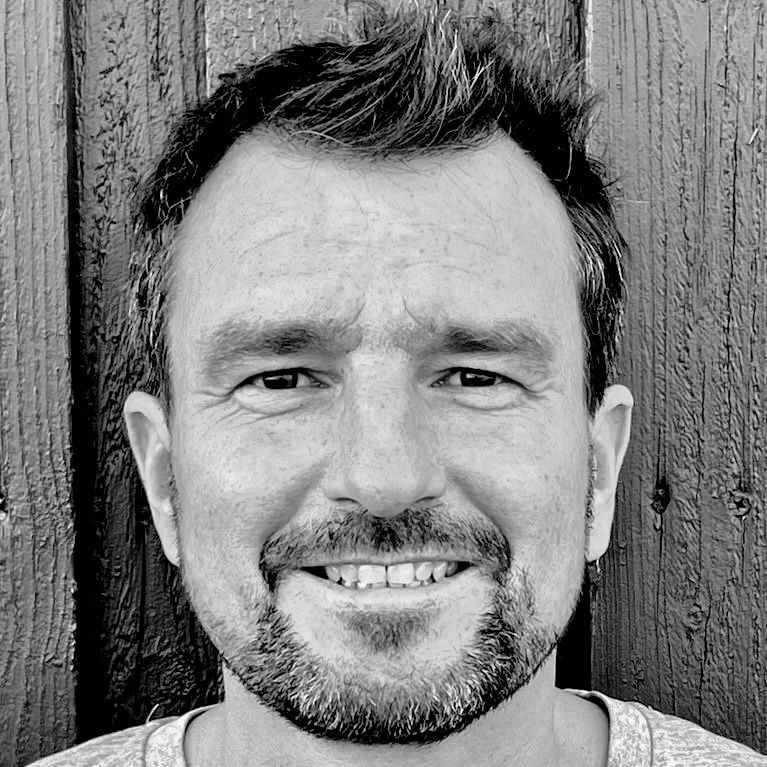 A man with a beard is smiling in a black and white photo.