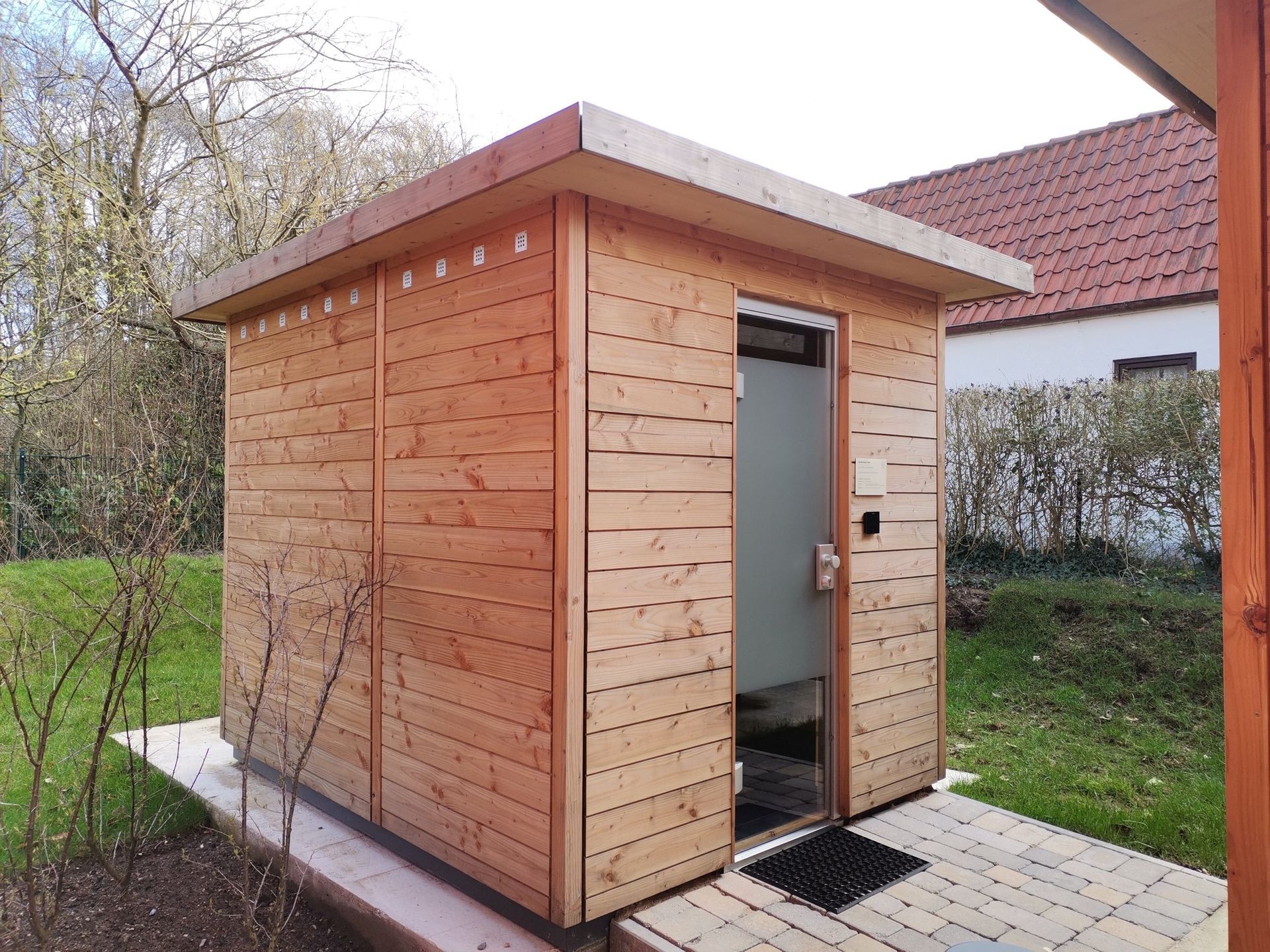 Ein Sauna-Haus aus Holz steht in einem Garten.