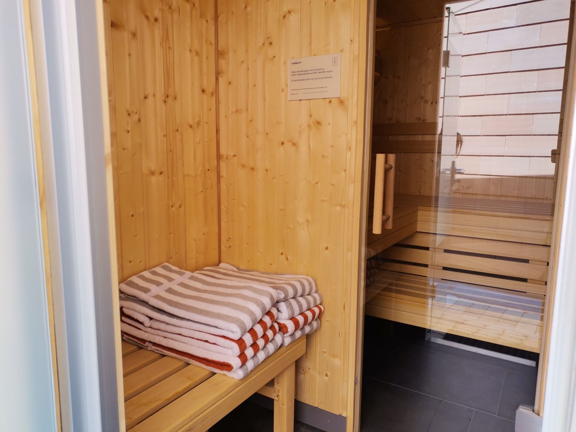 Eine Holzsauna mit Handtüchern auf der Bank und einer Glastür.