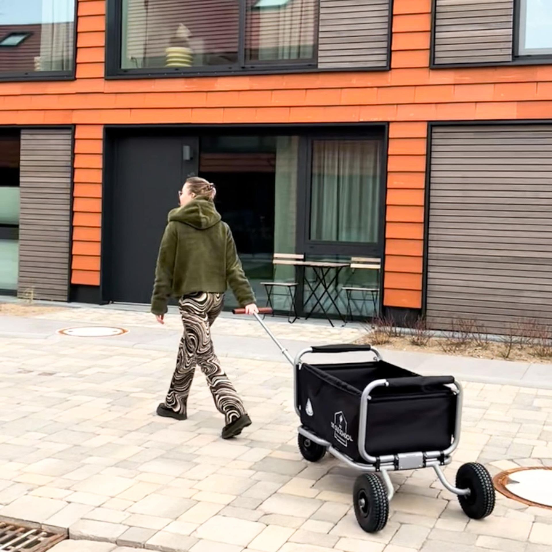 Eine Person zieht vor einem Gebäude einen Wagen mit einer schwarzen Tasche darauf.