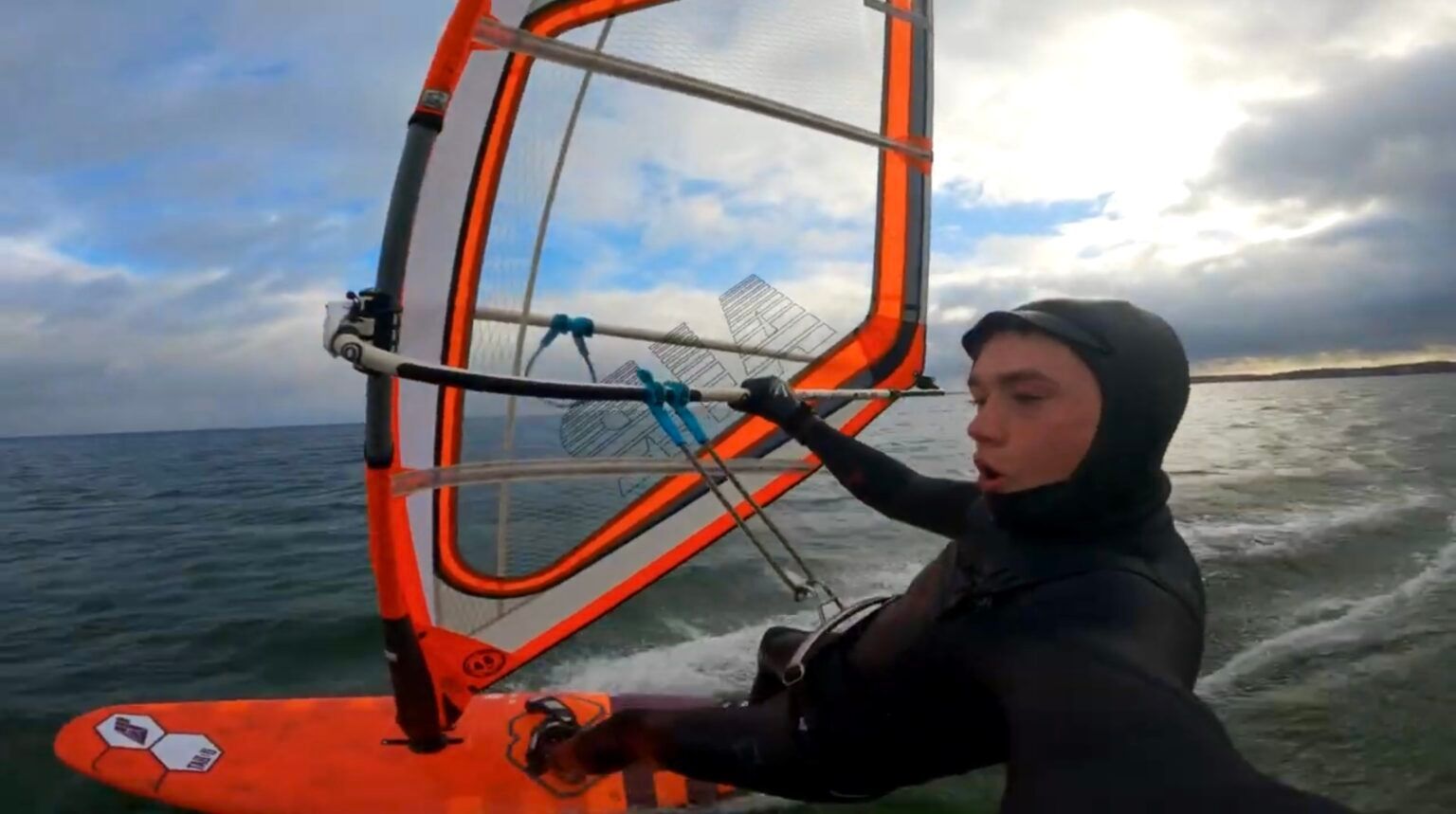 Ein Mann im Neoprenanzug windsurft im Meer.
