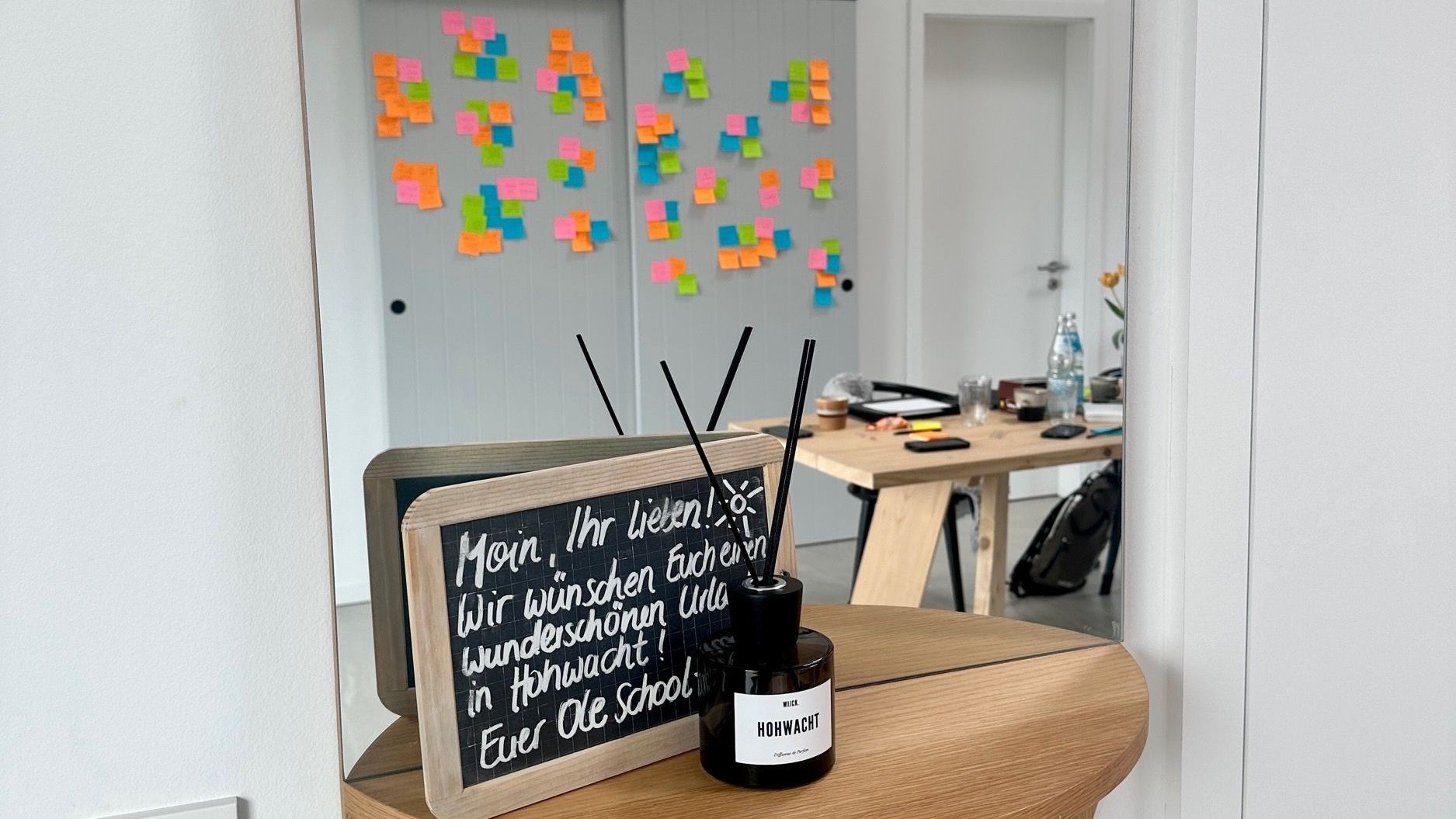 A sign on a table in front of a mirror with sticky notes on the wall.