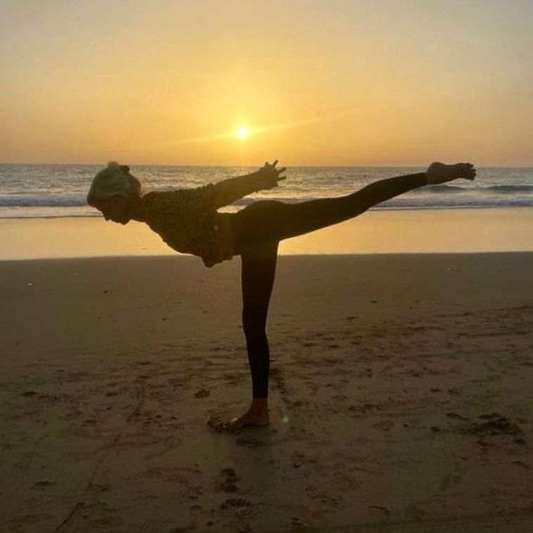 Eine Person macht bei Sonnenuntergang eine Yoga-Pose am Strand.