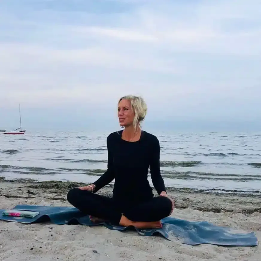 Eine Frau sitzt auf einer Yogamatte am Strand.