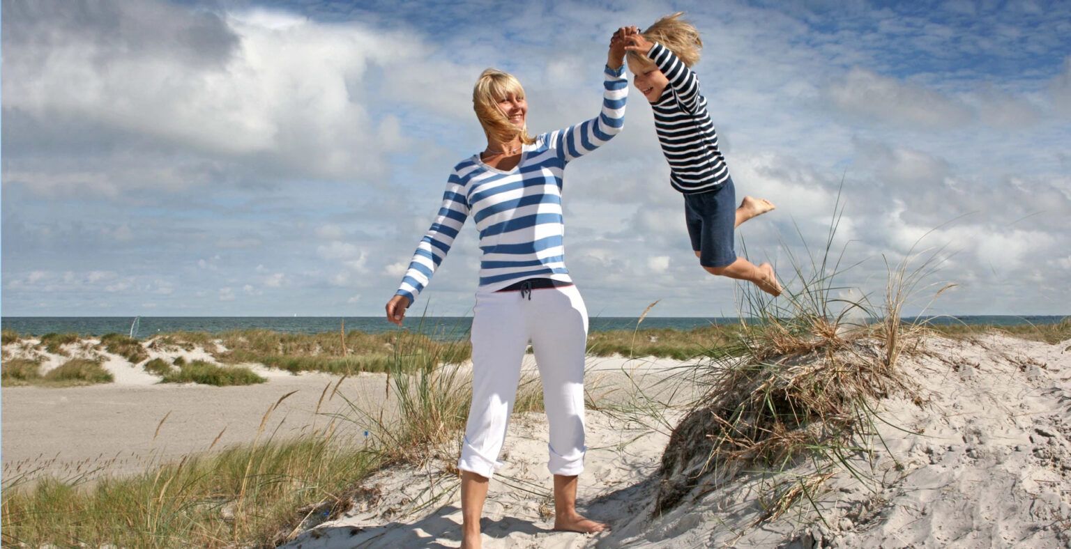 Eine Frau hält an einem Strand ein Kind in die Luft.