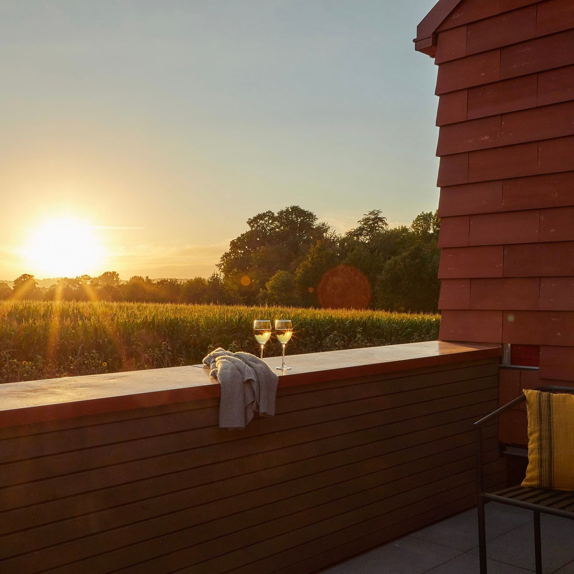 Zwei Gläser Wein stehen auf einer Balkonbrüstung mit Blick auf ein Feld bei Sonnenuntergang