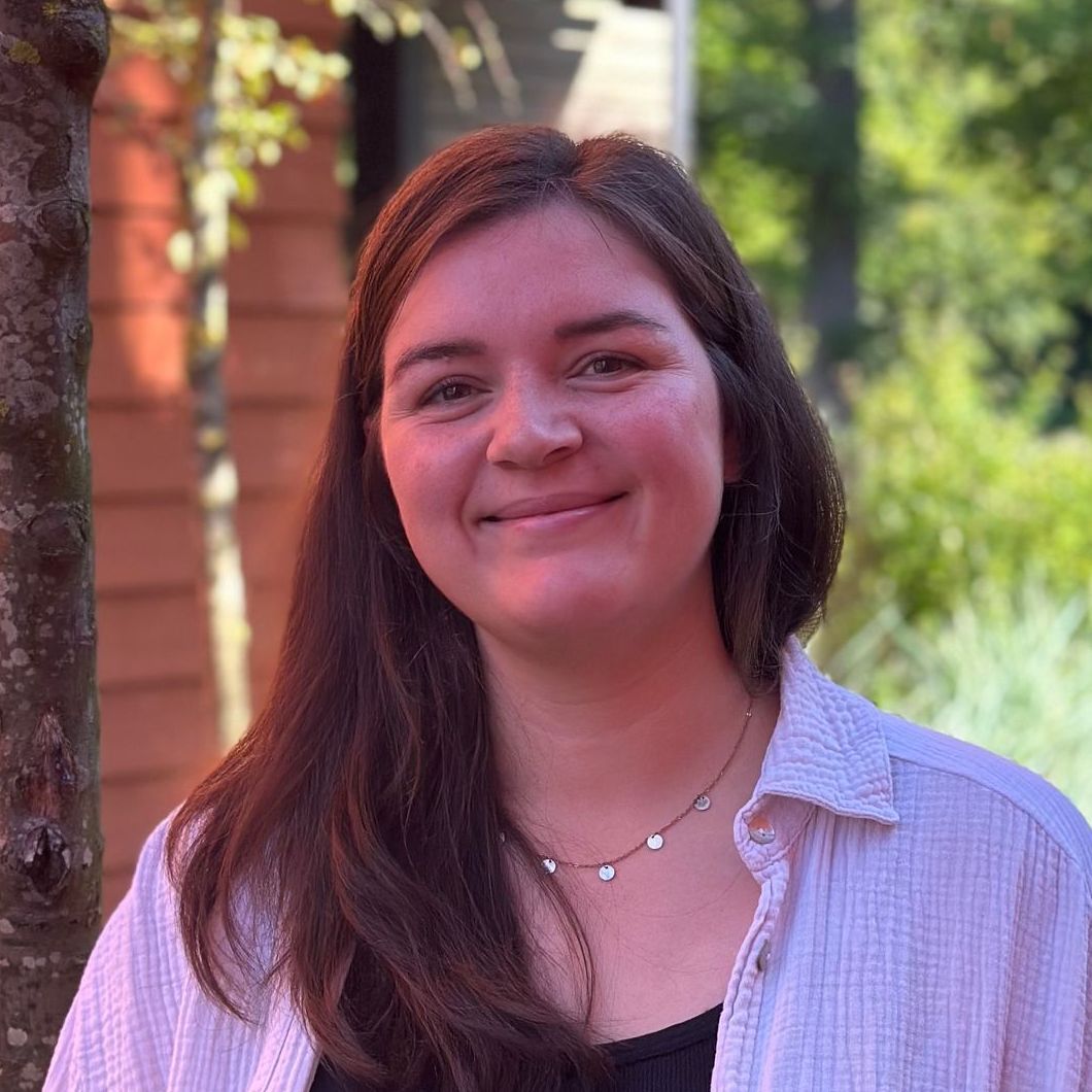 A woman is smiling for the camera while standing in front of a tree.