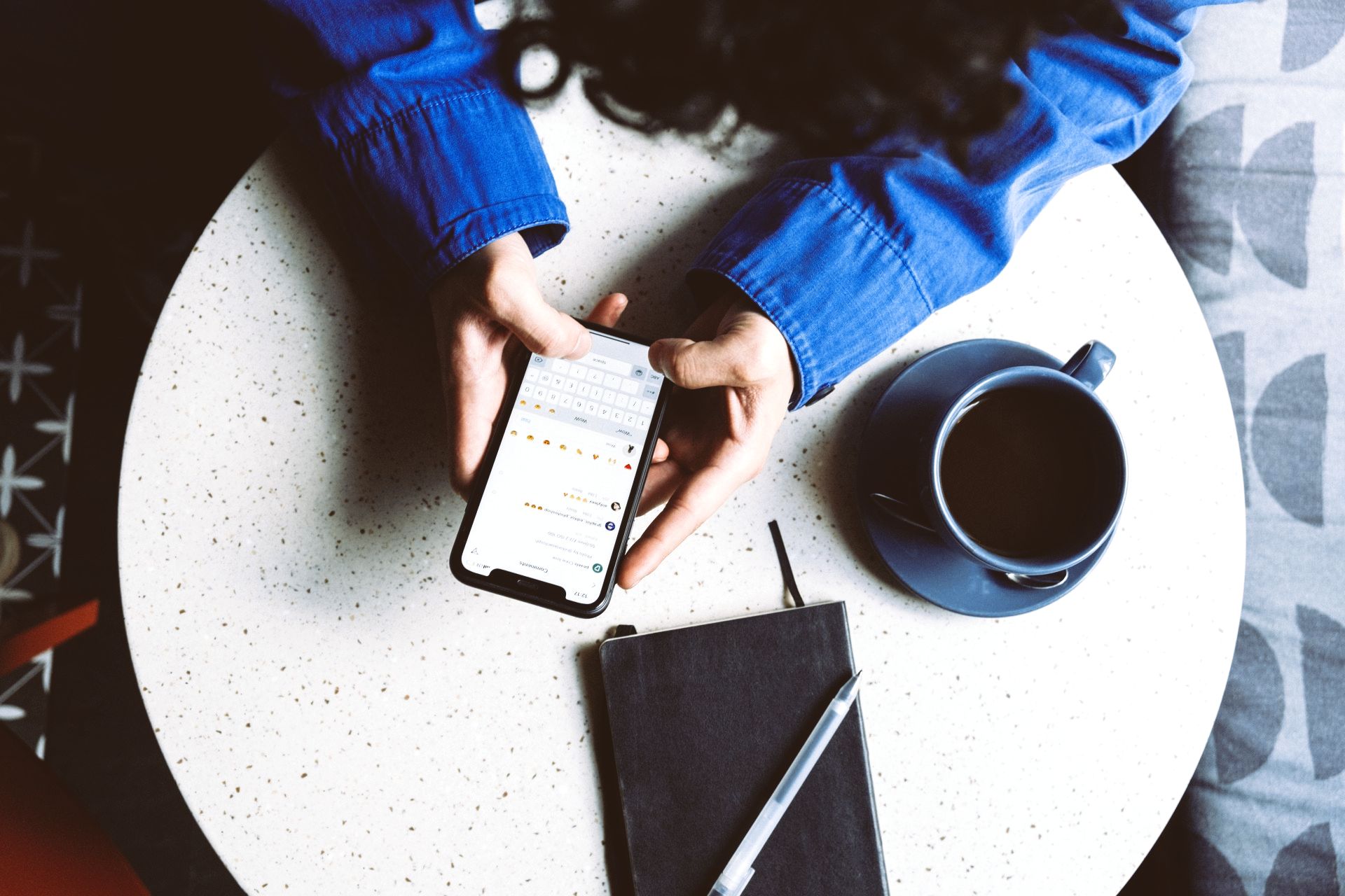 A person is sitting at a table with a cup of coffee and a cell phone.