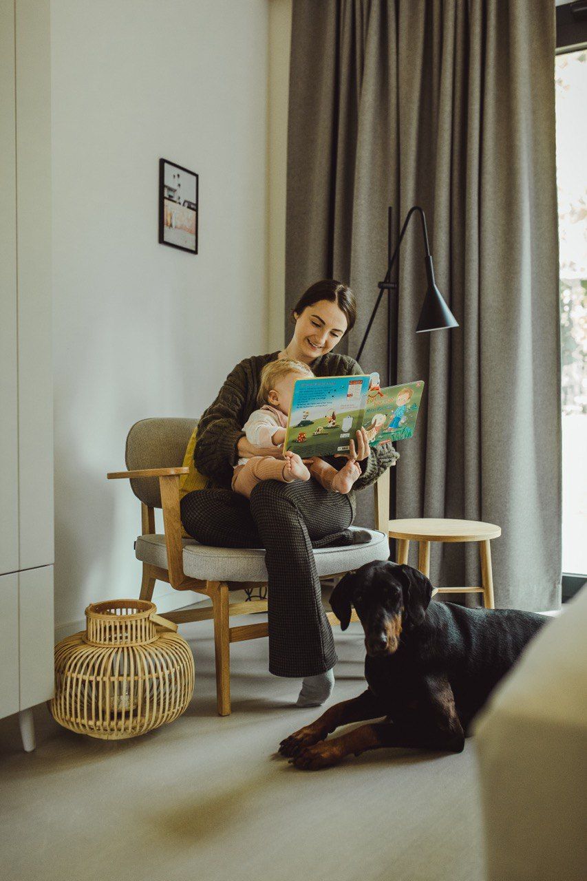 Eine Frau sitzt auf einem Stuhl, hält ein Baby und liest ein Buch.