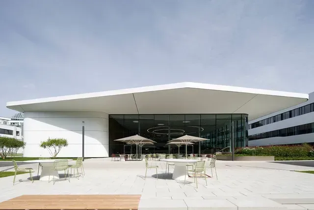 Ein großes weißes Gebäude mit Tischen und Stühlen von Paul Hartmann AG, Neubau Forum und Office.