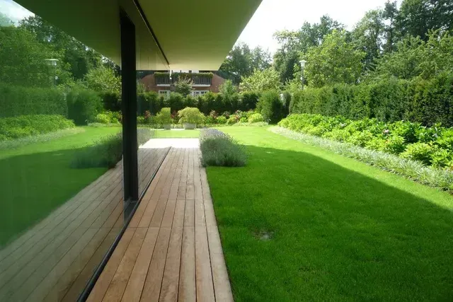 Ein üppiger grüner Rasen mit einem Holzdeck im Vordergrund vom Hausgarten in Erlangen