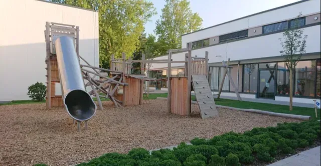 Ein Spielplatz mit Rutsche und Kletterwand vor einem Gebäude.