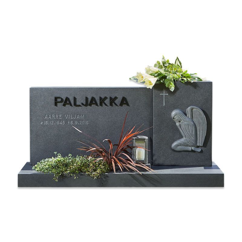 Tummanharmaa hautakivi, jossa kaiverrettu sydän, risti, kukkia ja pieni lyhty jalustalla