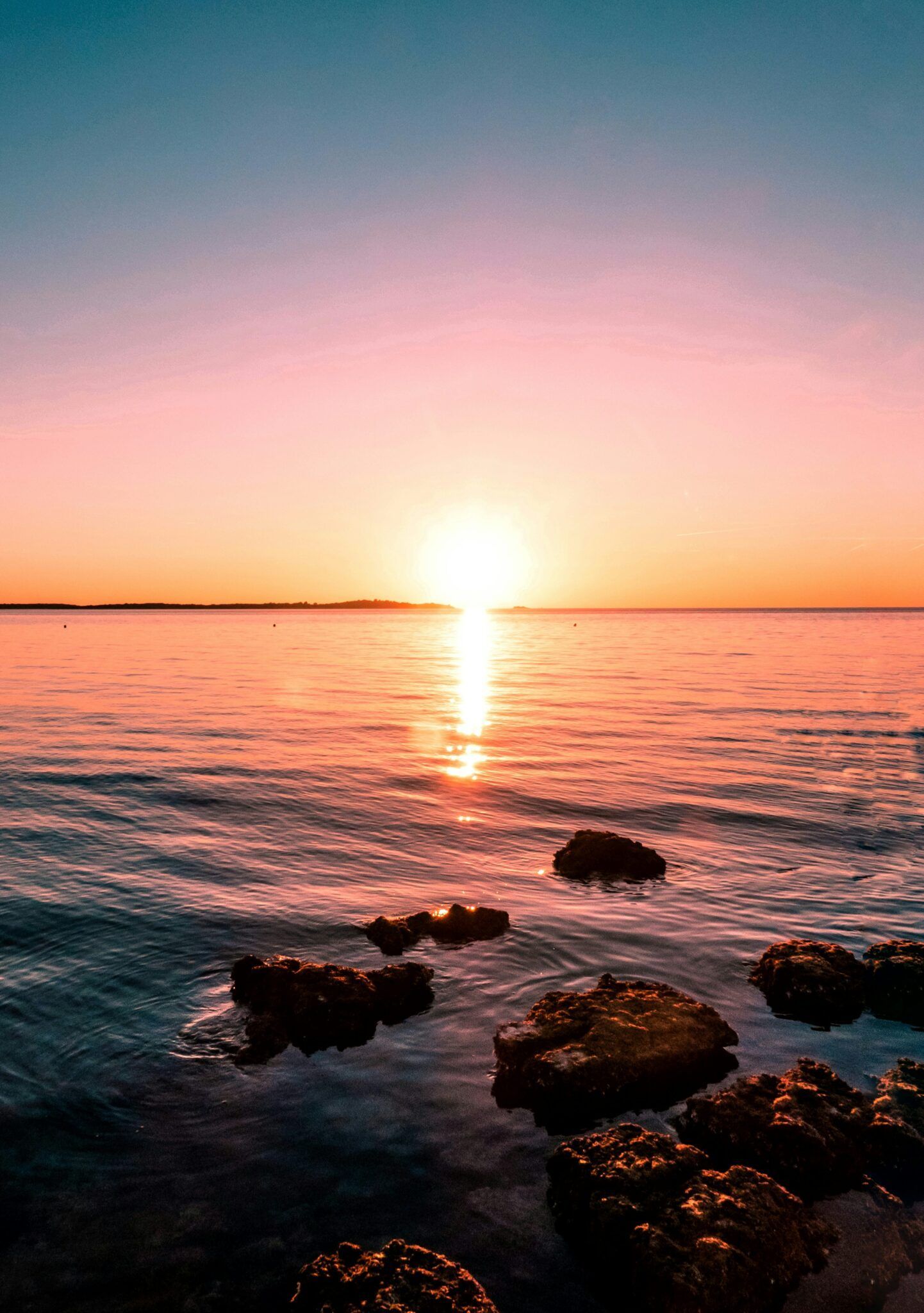Auringonlasku tyynen meren yllä kivisellä rannalla ja vaaleanpunaisen oranssilla taivaalla