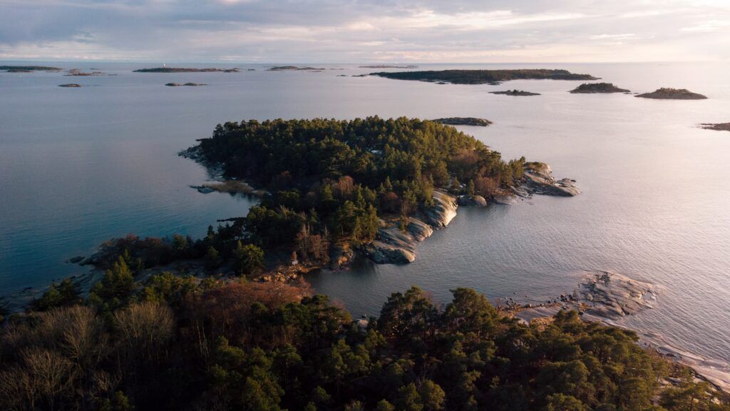 Ilmakuva rehevästä saaresta, jota ympäröi tyyni, heijastava vesi auringonlaskun aikaan